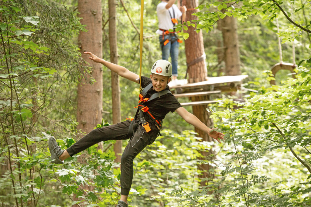 Ein kleiner Junge mit Kletterhelm macht einen Flying Fox und fliegt in der Luft.