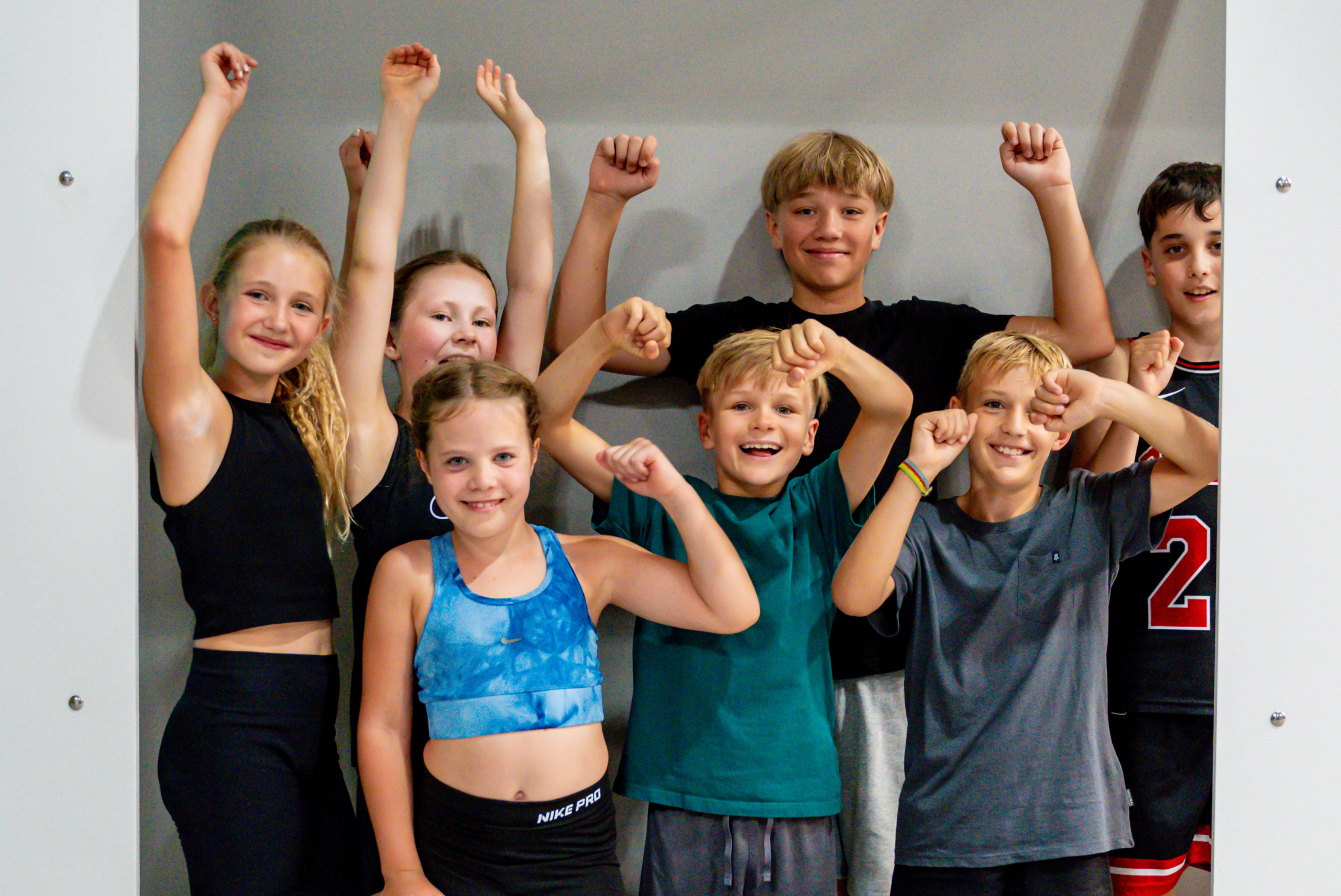 Eine Gruppe von sechs Kindern in Sportkleidung posieren gemeinsam und heben triumphierend die Arme.