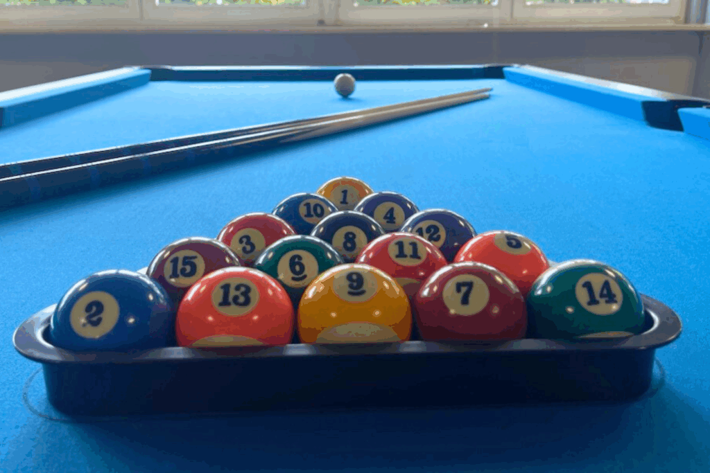 Billard Kugeln sind in einem Dreieck plaziert mit Queues auf einem Billard Tisch welcher blau ist.