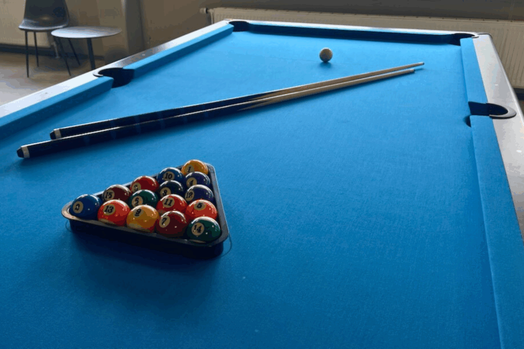 Billard Kugeln sind in einem Dreieck plaziert mit zwei Queues auf einem Billard Tisch welcher blau ist.