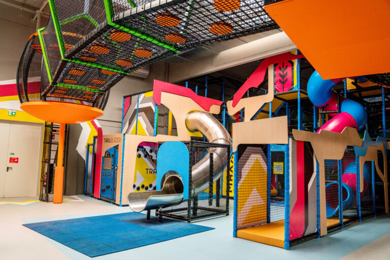 Ein Indoor Spielplatz aus bunten Rutschen, interaktiven Spielen, einem Labyrinth mit Netz außen. Aufgeteilt in drei Ebenen.