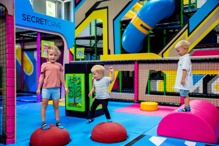 Drei kleine Kleinkinder spielen in der Toddler Area. Sie hüpfen auf kleinen roten Kreisen und pinken Schaumstoff Hindernissen.