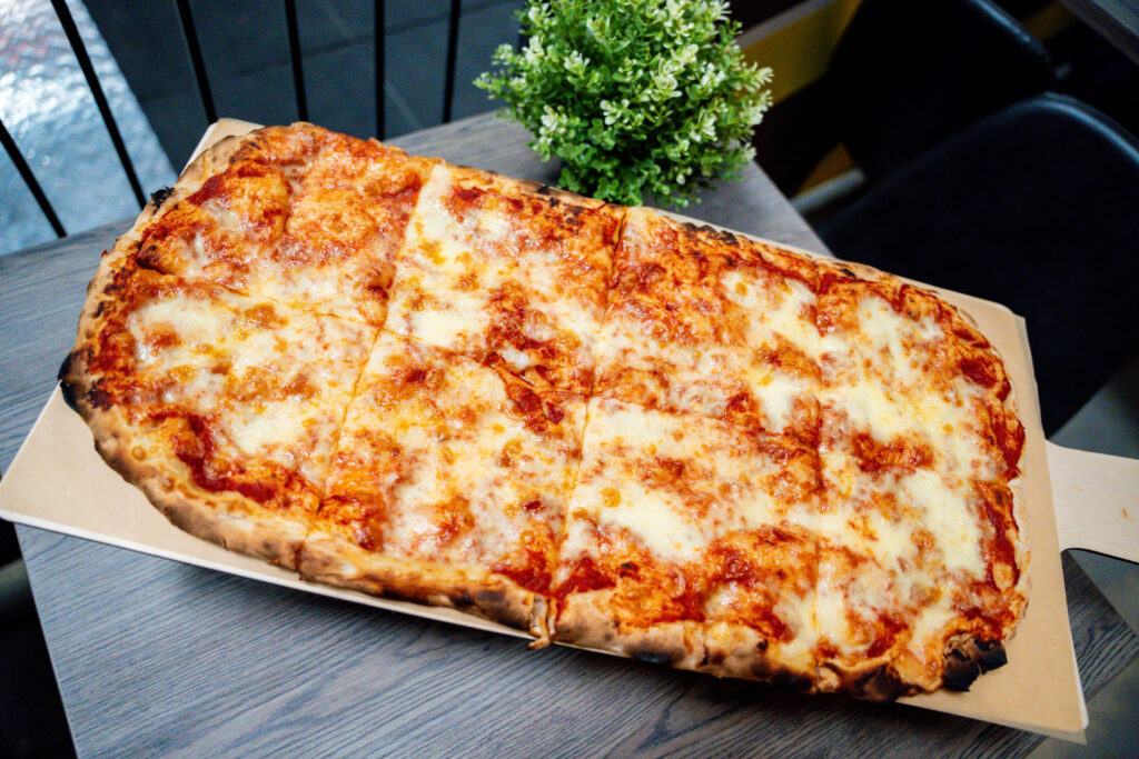 Pizza Margherita auf einer Holzschaufel, im Hintergrund eine grüne Pflanze.