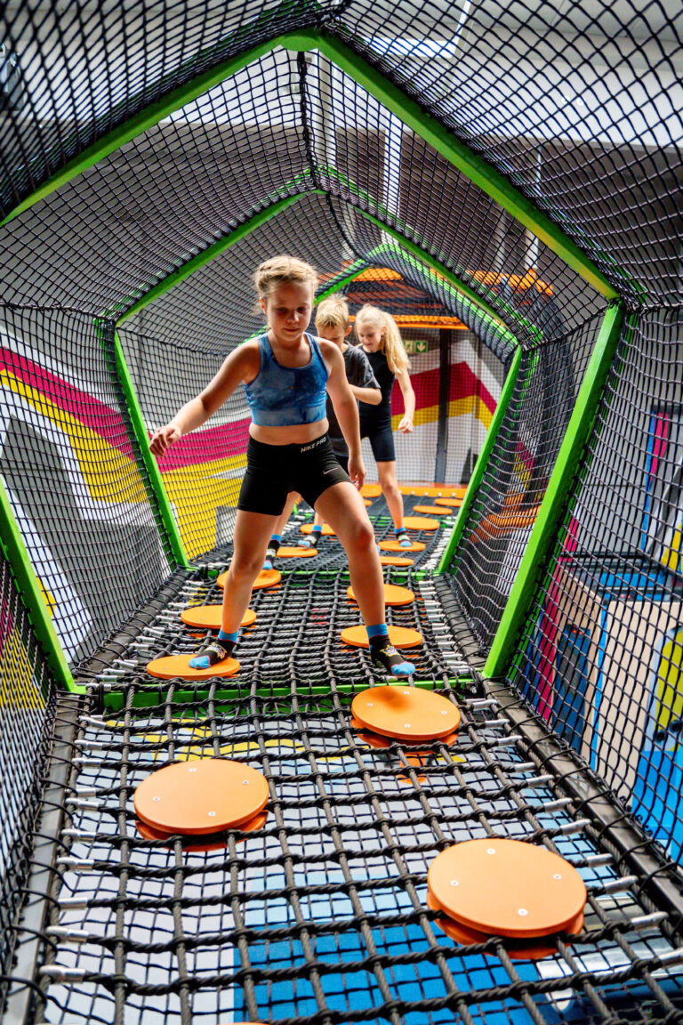 Drei junge Mädchen mit geschlossenen Haaren balancieren auf orangenen Kreisen in einem Höhenlabyrinth. Sie gehen hintereinander und konzentrieren sich, dass sie auf die orangenen Kreise treten.