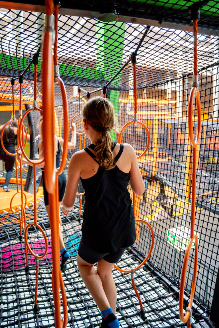 Kleine Mädchen gehen durch einen Hindernissenparcours aus orangenen Reifen in der Luft in einem Höhenlabyrinth.