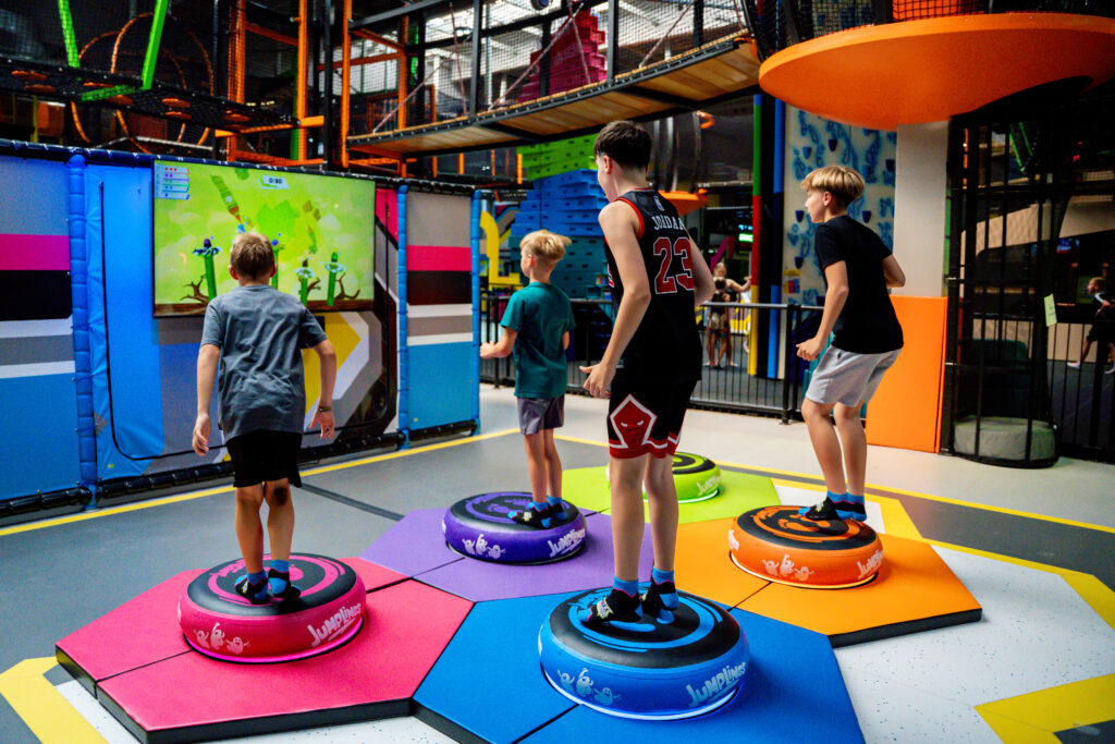 Kinder stehen auf verschieden farbigen runden Kreisen. Auf diesen kann man hüpfen. Vor den Kreisen ist im Hintergrund ein Bildschirm, auf welchem ein Videospiel abgespielt wird. Die digitalen Spielfiguren werden je nach Bewegung auf dem runden Kreis gesteuert.