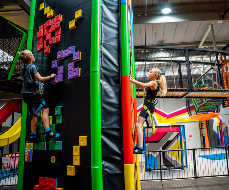 Zwei Kinder klettern gegenüber eine Wand nach oben. Beide sind gesichert.