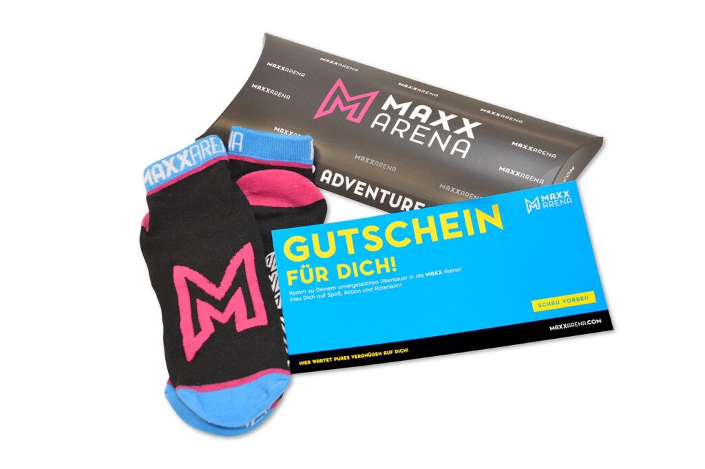 Geschenkartikel sind abgebildet: MAXX Socks, eine Gutschein-Box mit Logo sowie eine Wertgutschein-Karte. Alle sind in den MAXX Arena Farben.