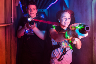 Zwei Jungedliche laufen mit ihren Laserball Phasern durch eine Arena.