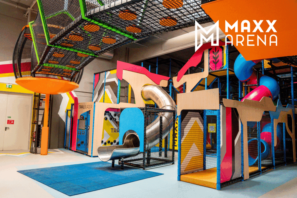 Ein Indoor Spielplatz aus bunten Rutschen, interaktiven Spielen, einem Labyrinth mit Netz außen. Aufgeteilt in drei Ebenen.