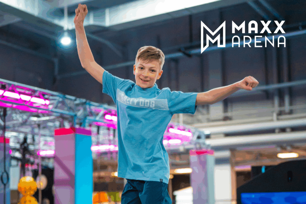 Ein Junge in türkisenen T-Shirt und Hose springt Trampolin und reißt die Hände in die Höhe während er lächelt.