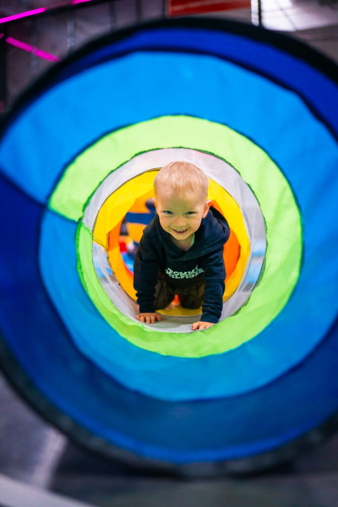 Es ist ein Junge zu sehen, welcher grinsend durch einen Zaubertunnel für MAXX Minis krabbelt.