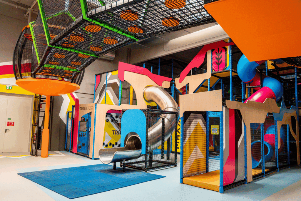 Ein Indoor Spielplatz aus bunten Rutschen, interaktiven Spielen, einem Labyrinth mit Netz außen. Aufgeteilt in drei Ebenen.