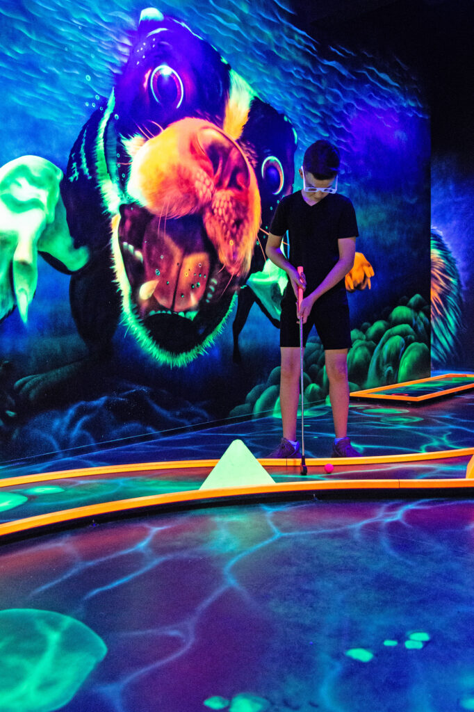 Ein junge spielt 3D Blacklight Golf und trägt deshalb eine 3D Brille und hält einen Golfschläger in der Hand.