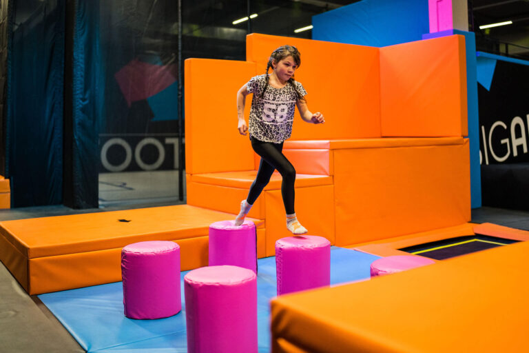 Ein kleines Mädchen mit leoparden T-Shirt geht über pinke Hinternissen auf einer großen Trampolinfläche.