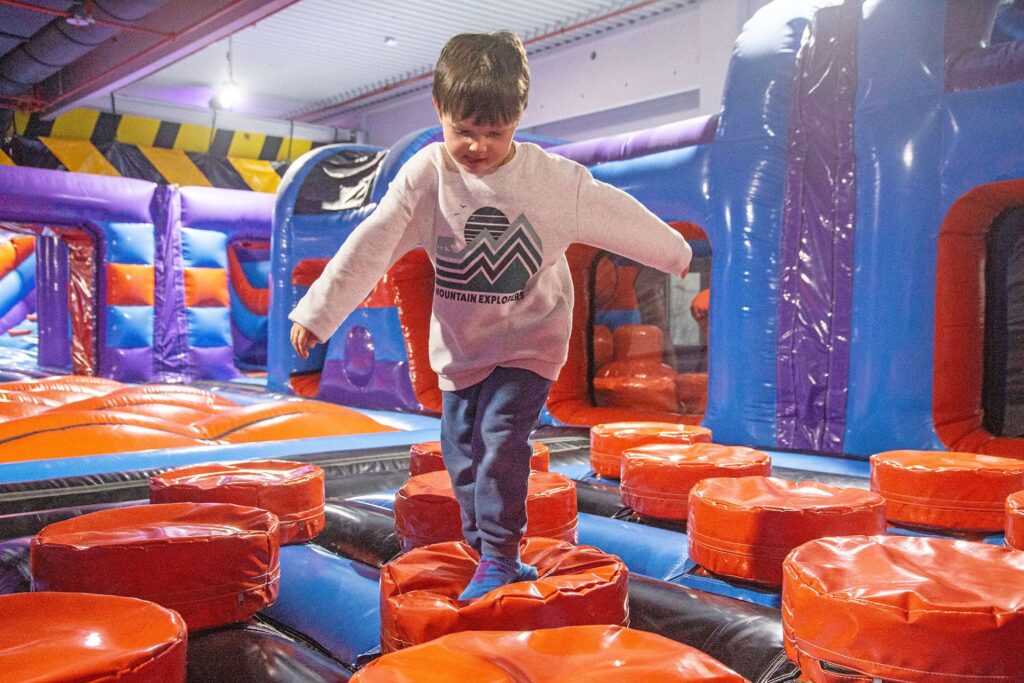 Ein kleiner Junge geht über rote Hinternisse in einer Hüpfburg für Kinder. Er sieht dabei sehr glücklich und konzentriert aus.