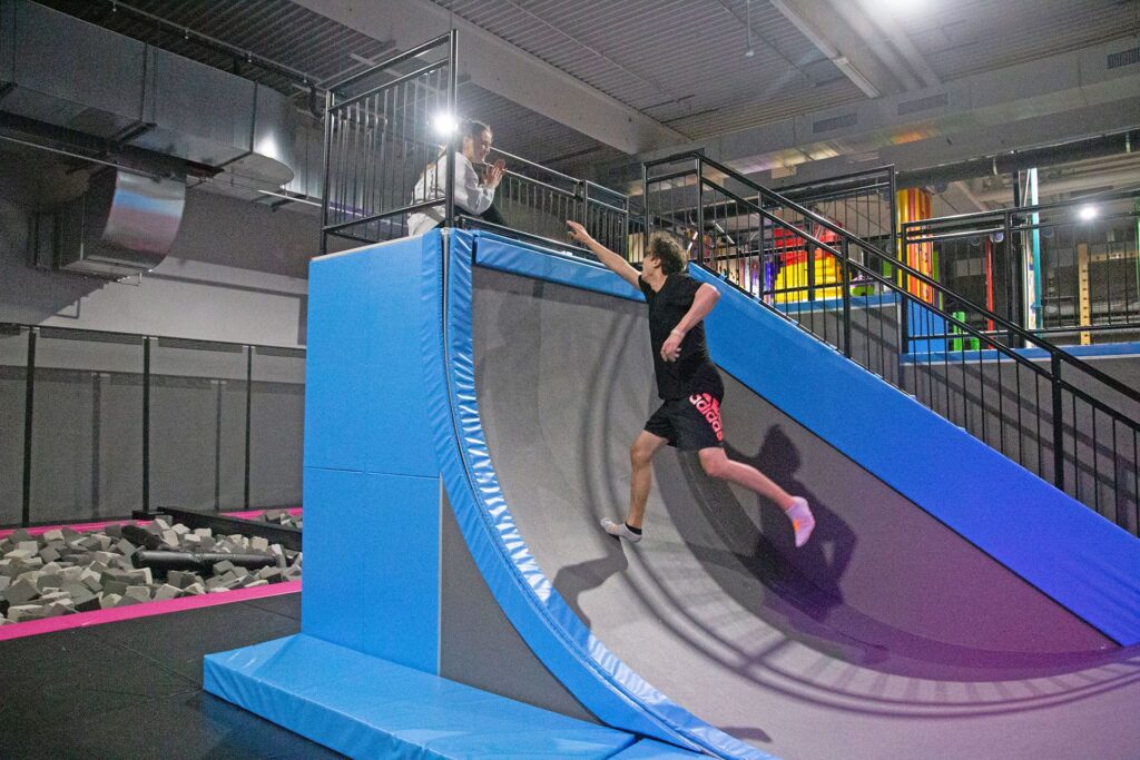 Ein Erwachsener Mann läuft eine 3 Meter Höhe Wand hinauf, welche sich The Wall in der Trampolinhalle nennt.