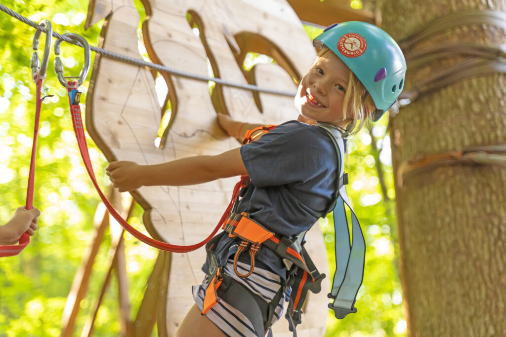 Ein kleines Mädchen mit Kletterhelm macht einen Parcour.