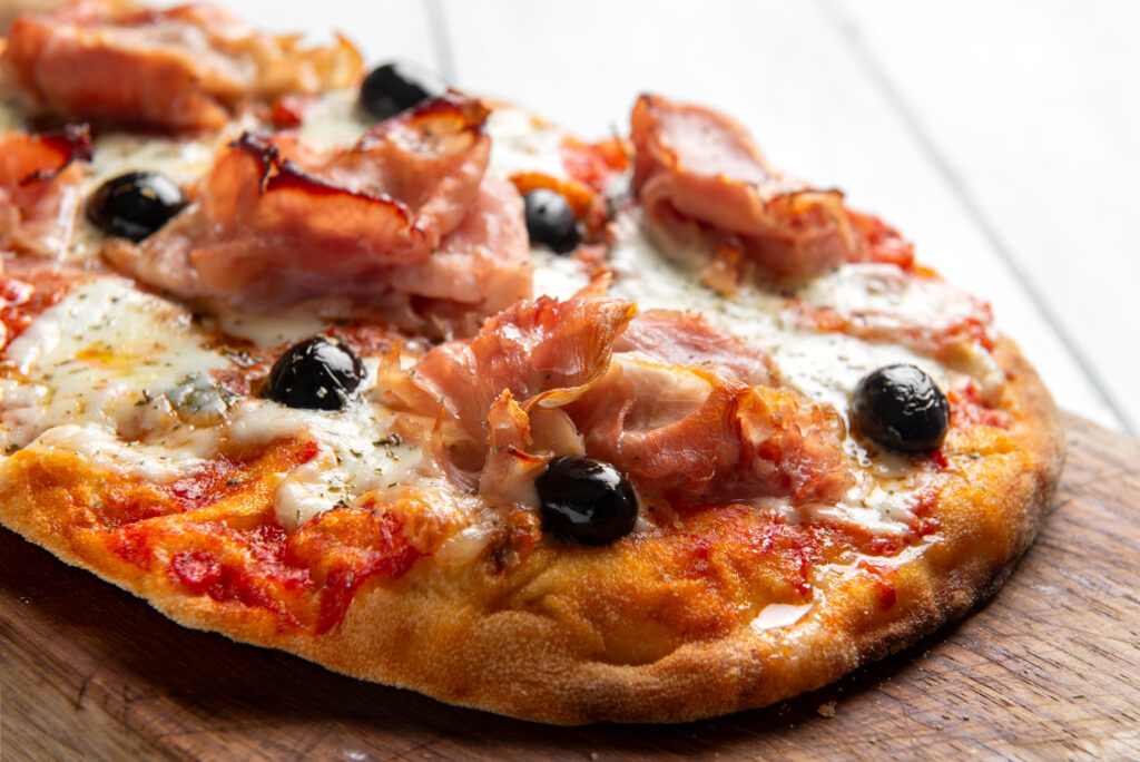Eine frisch gebackene Pinsa romana con prosciutto, mozzarella, sugo e olive nere, cibo italiano auf einem Holzbrett.